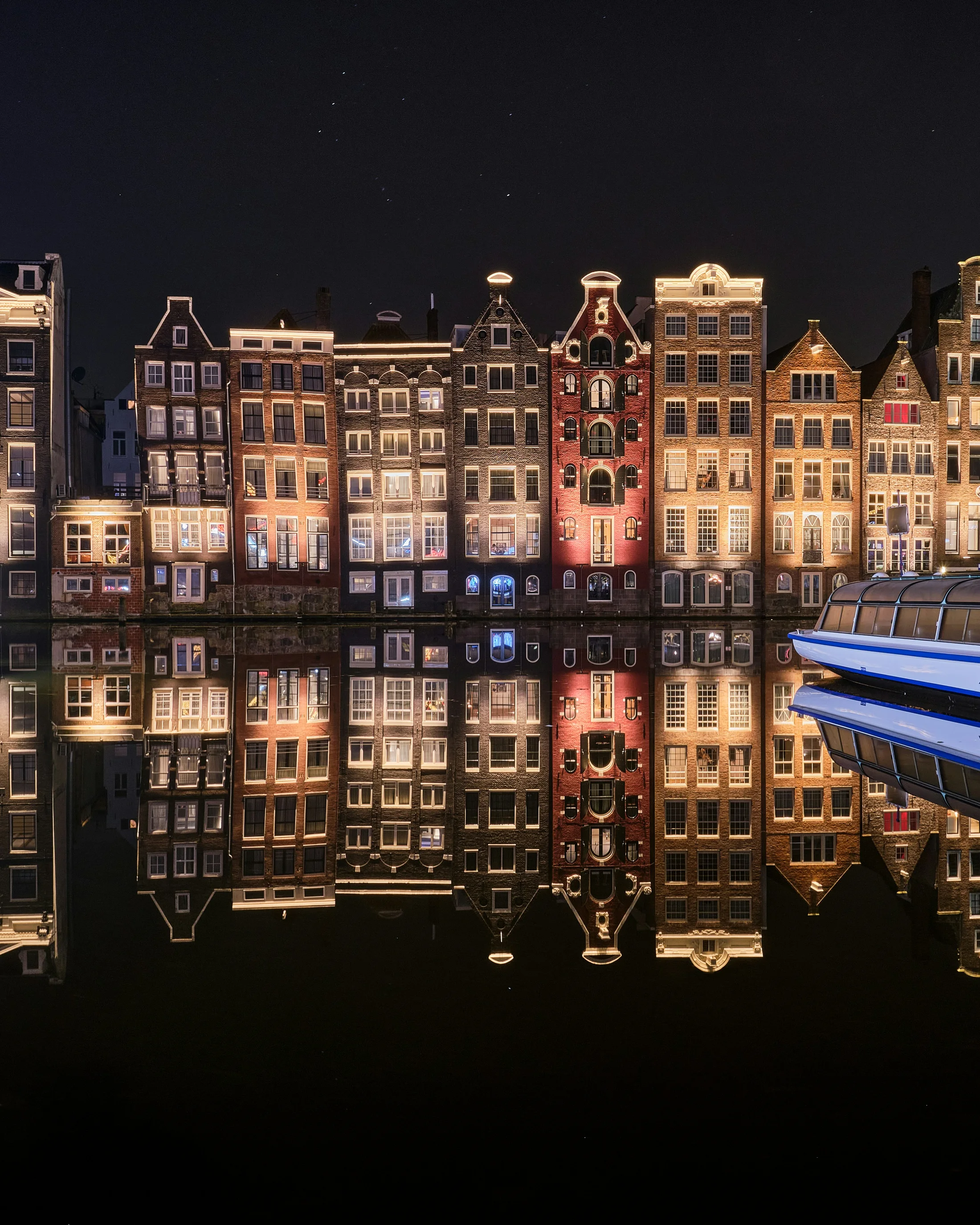 Illuminated Amsterdam canal houses reflected in dark water at night