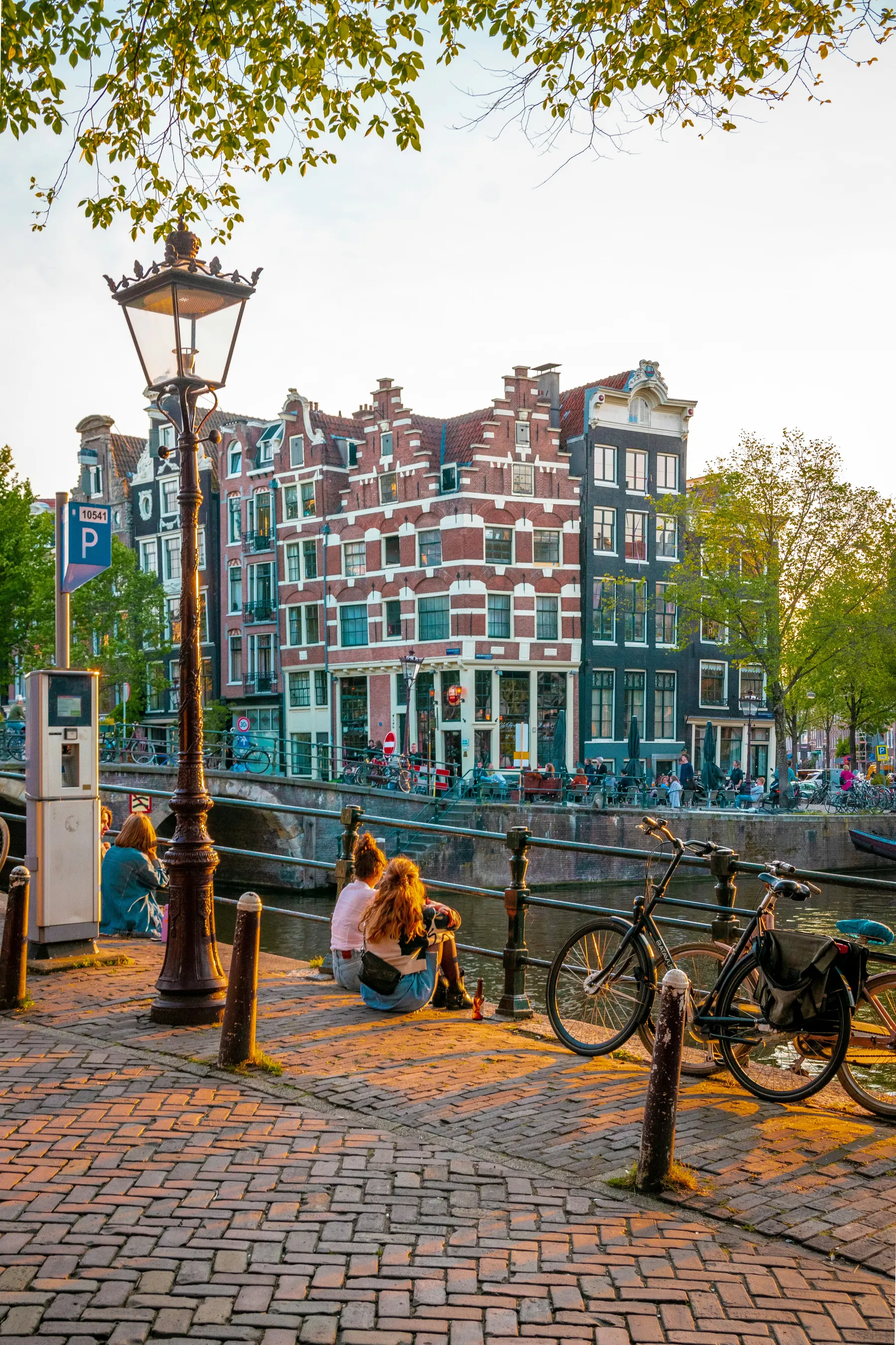 People sitting beside an Amsterdam canal with bicycles and brick houses nearby