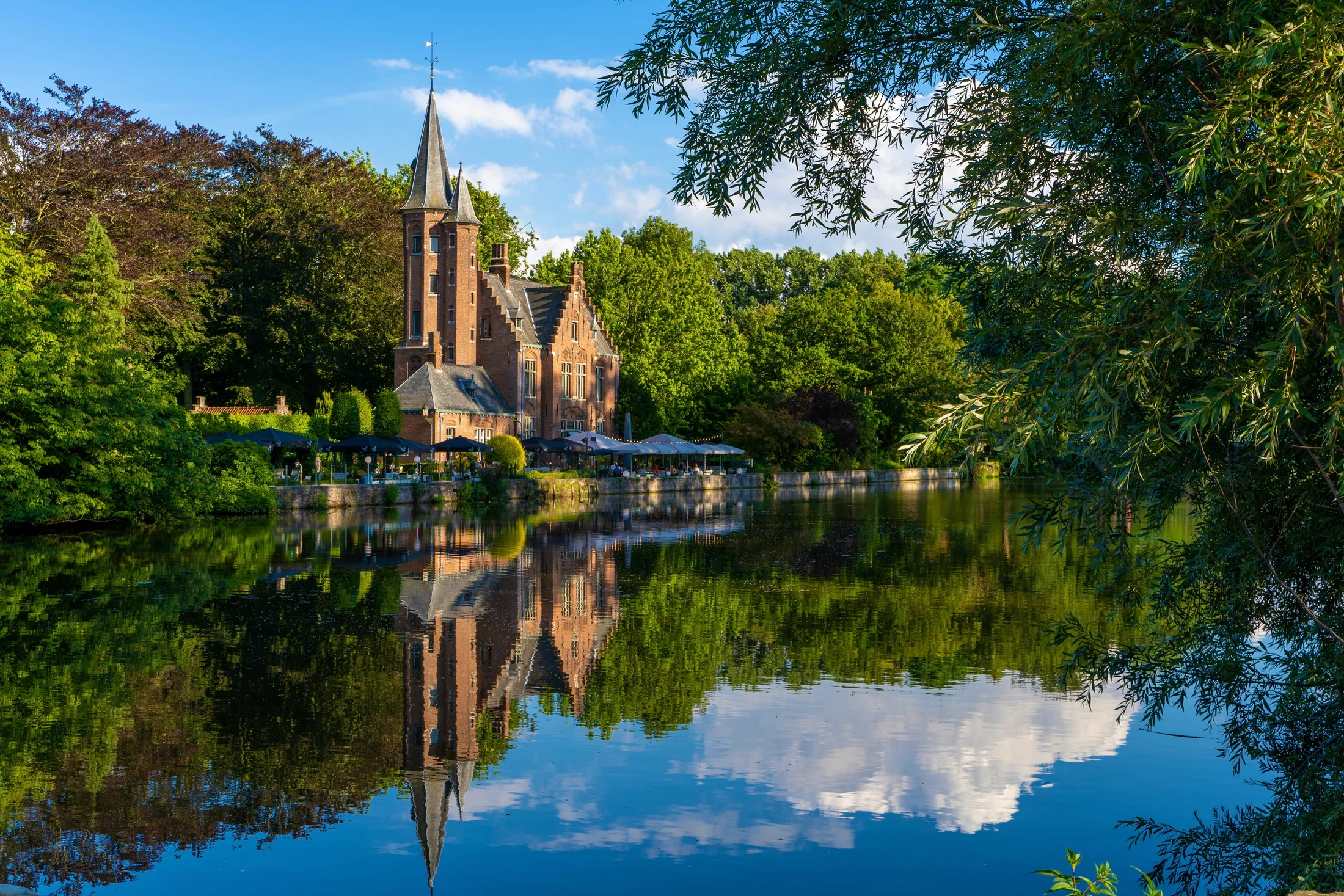 Quiet Bruges canal with trees, a church tower, and reflections in the water