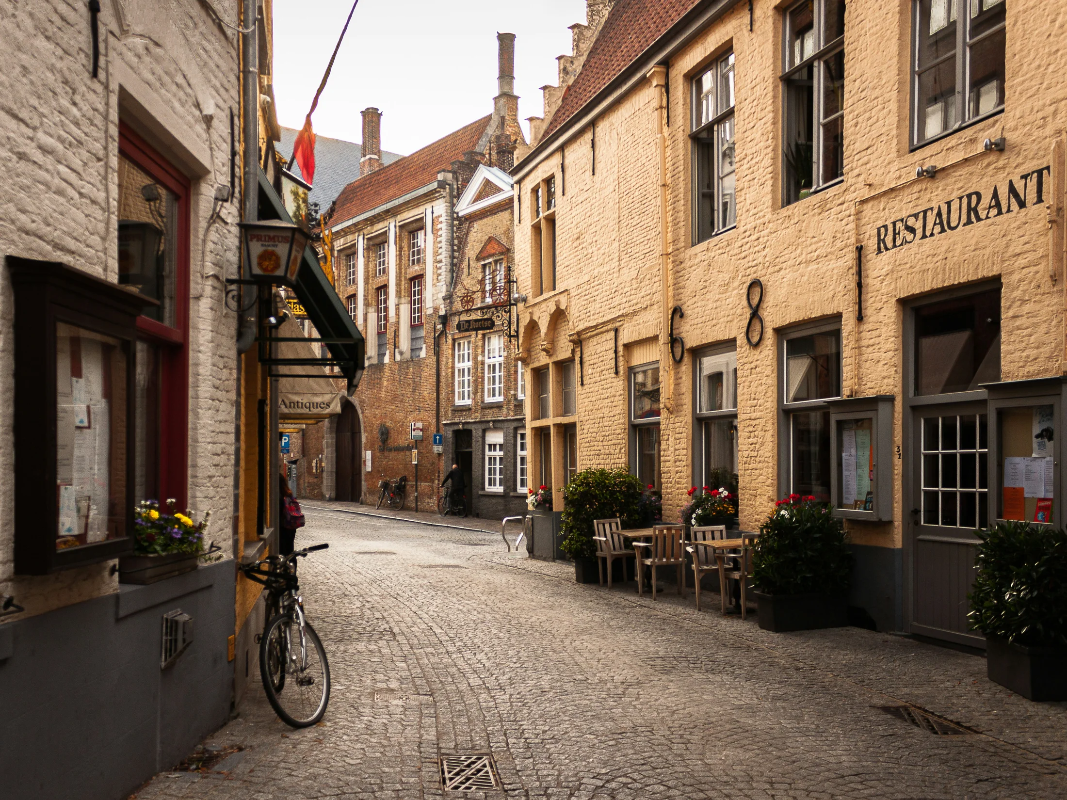 Quiet cobbled street in Bruges with old brick buildings and restaurant signs